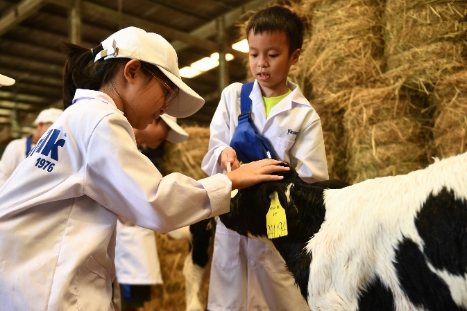 A group of kids in white coats petting a goat  Description automatically generated